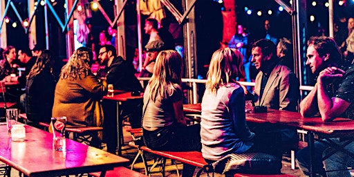 Singles im Gespräch an langen Tischen in einer Bar mit Lichterketten